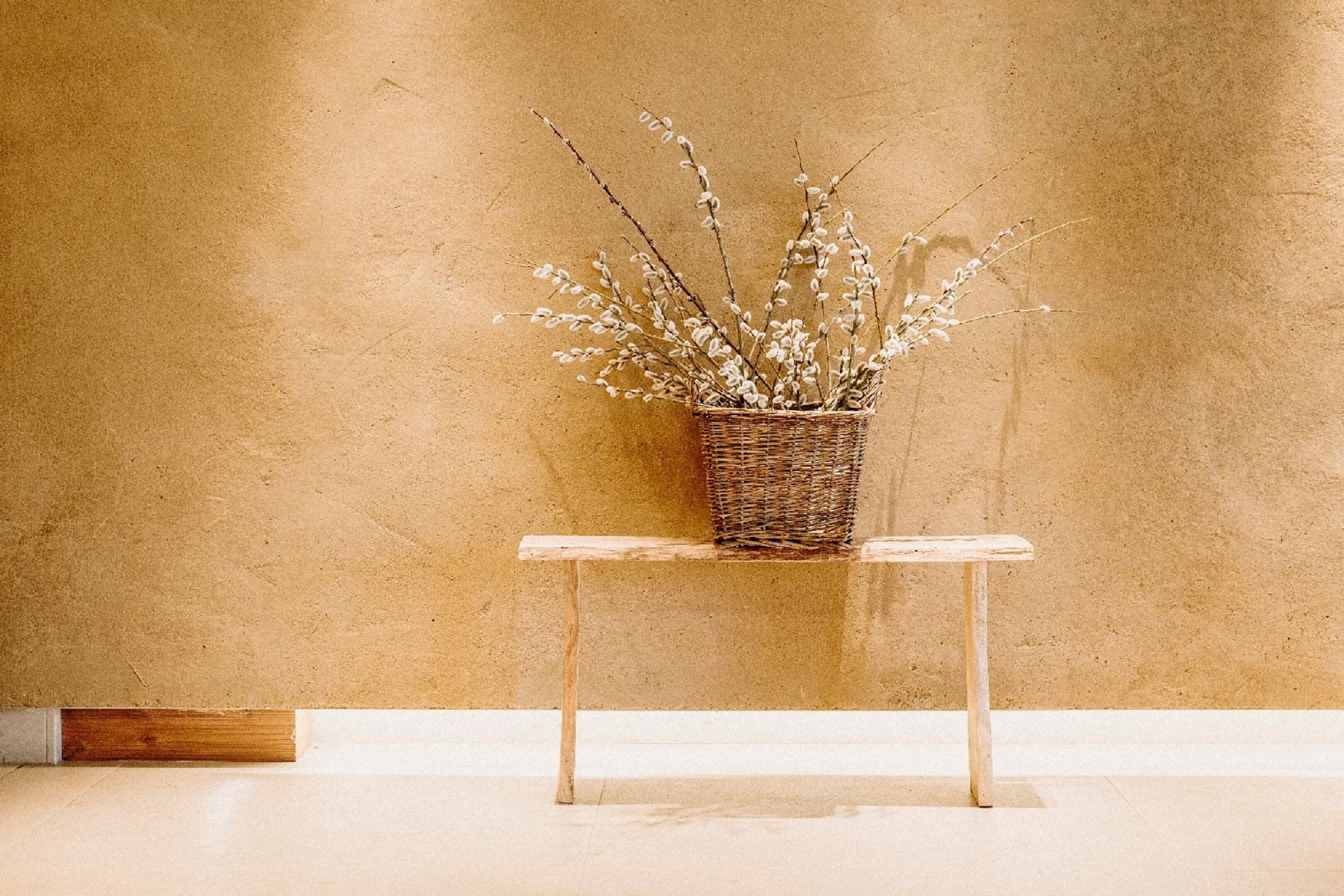 A wicker basket with branches on a wooden bench against a textured wall.