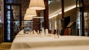 A dining area with a long table set for a meal, featuring hanging pendant lights and a textured wall in the background. - Kurhotel San Andreas (Bad Fuessing)