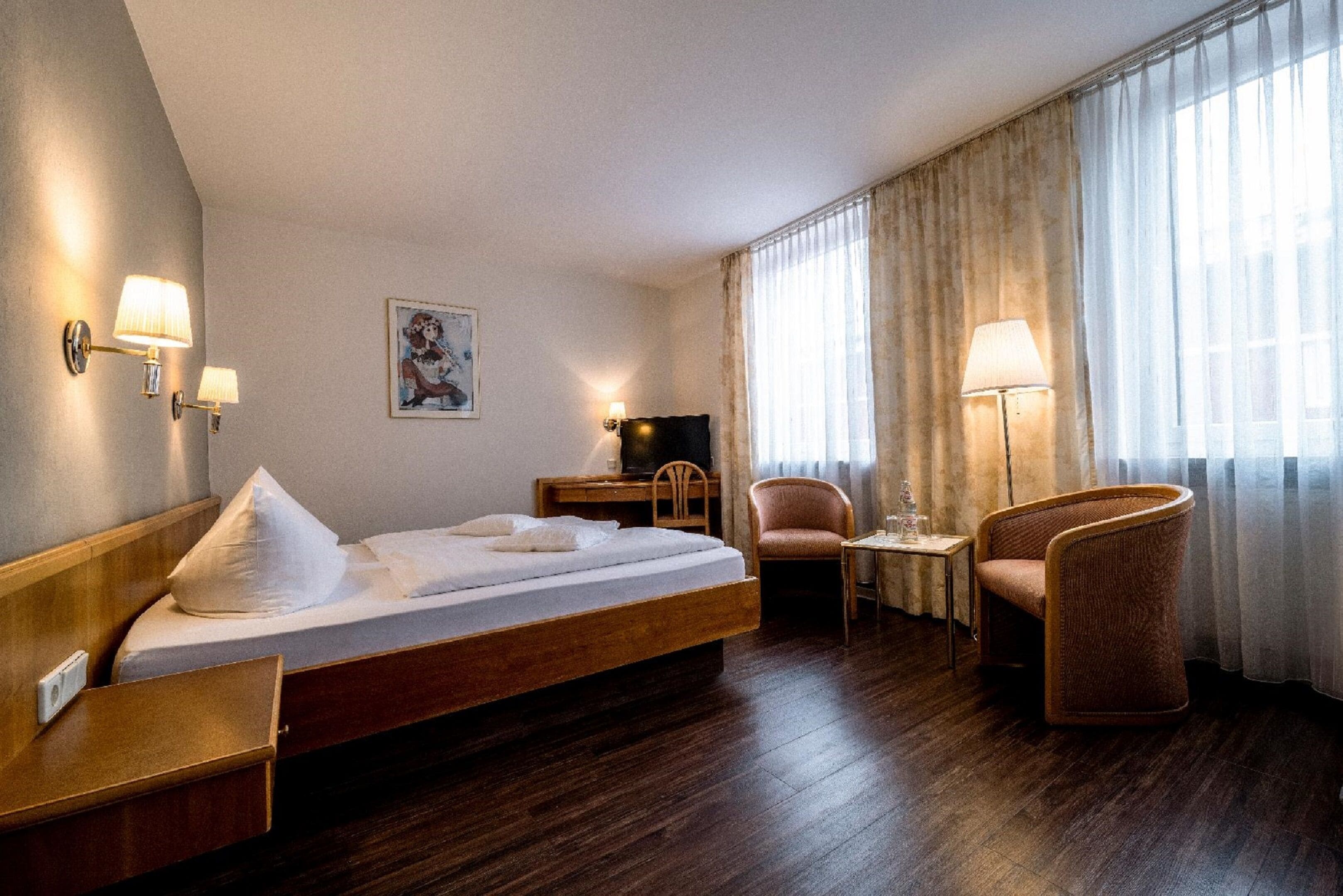 Habitación de hotel con una cama de madera, un escritorio, una silla y una lámpara.