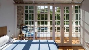 A bedroom with a large bed, a wooden floor, a stone wall, and a sliding glass door leading to an outdoor area. - "Apartamentos Bestarruza" - 2 rooms (Mugardos)