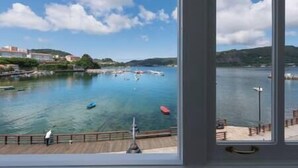 A view from a window overlooking a calm body of water with boats, a wooden dock, and buildings in the background. - "Apartamentos Bestarruza" - 2 rooms (Mugardos)