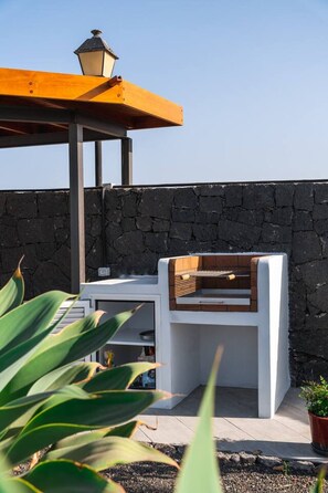 An outdoor seating area with a stone wall, a wooden bench, and a table under a yellow umbrella. - Villa con Piscina Cerca de Playa Papagayo (Playa Blanca)