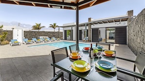 A modern outdoor dining area with a pool and lounge chairs.