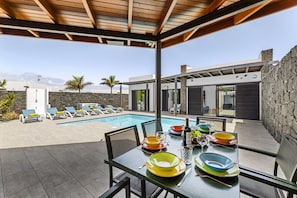 A modern outdoor dining area with a pool and lounge chairs.