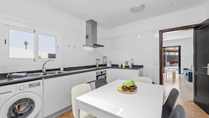 A modern kitchen with a built-in washer, a dining table with chairs, and a view of the outside through large windows.