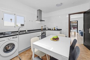 A modern kitchen with a built-in washer, a dining table with chairs, and a view of the outside through large windows.