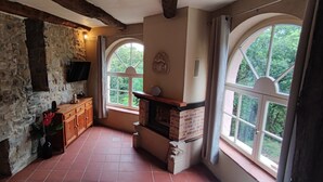 A rustic kitchen with stone walls, a wooden cabinet, a brick fireplace, and large windows with a view of greenery. - Cévennes vacations in the heart of nature in a farmhouse apartment (Cendras)