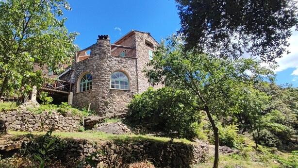 A stone building with arched windows and a chimney, surrounded by trees and greenery. - Cévennes vacations in the heart of nature in a farmhouse apartment (Cendras)