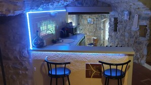 A stone-walled kitchen with a modern bar area, two bar stools, and a view into the adjacent dining area. - Cévennes vacations in the heart of nature in a farmhouse apartment (Cendras)