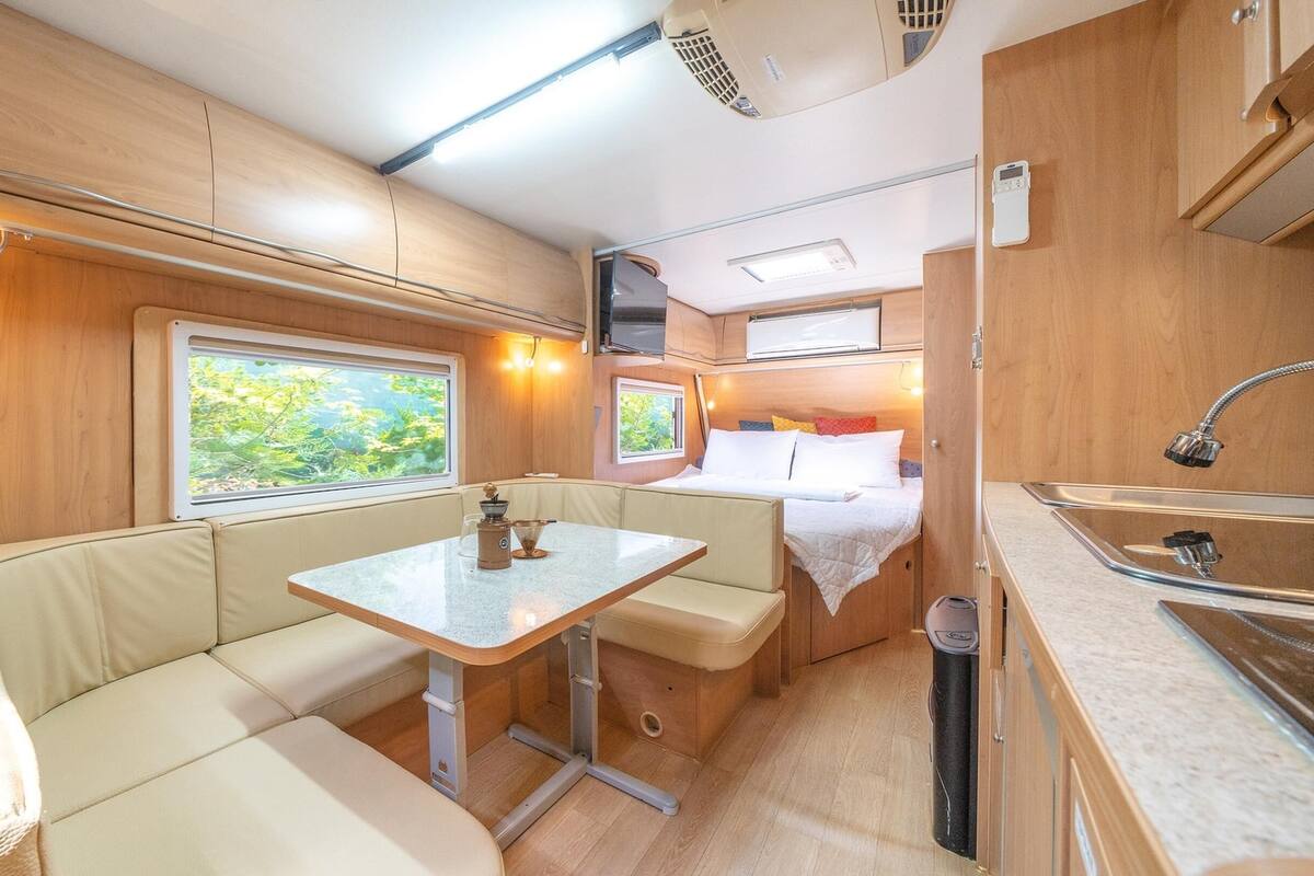A compact RV interior with a kitchenette, a dining area, and a sleeping berth.