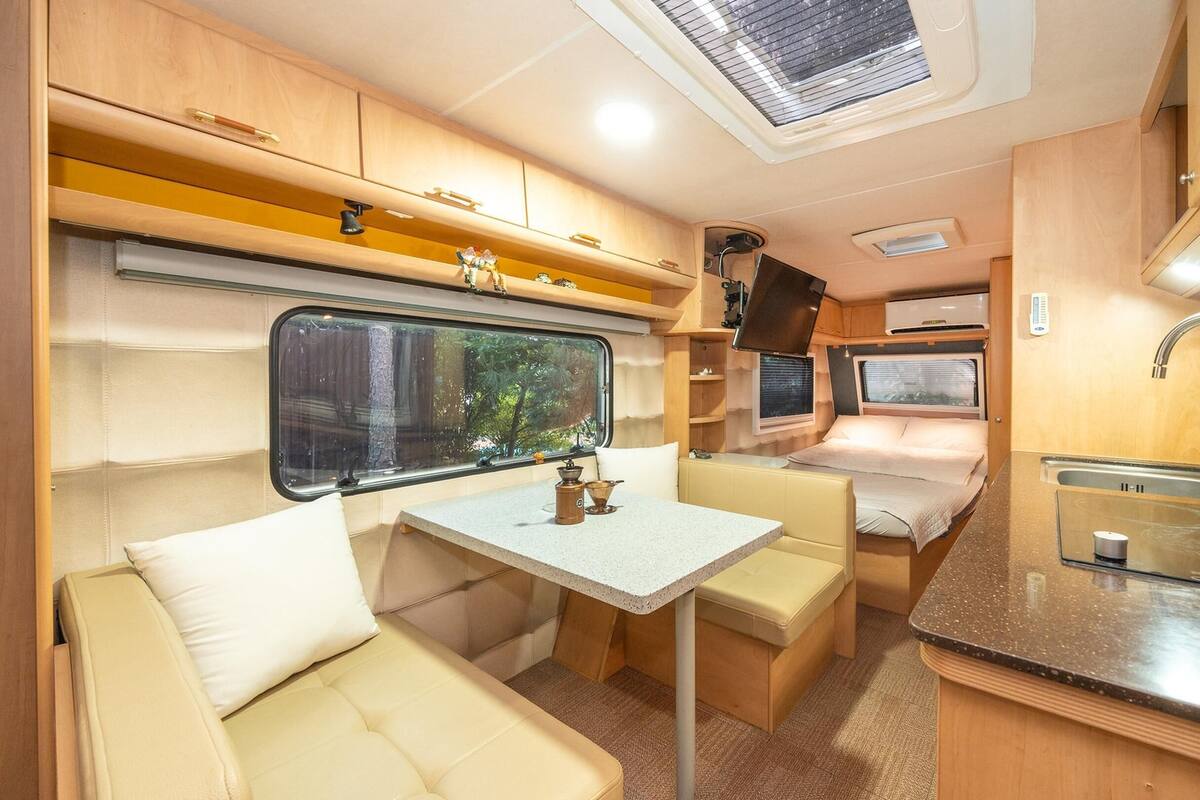 A compact RV interior with a kitchenette, a dining area, and a sleeping berth.