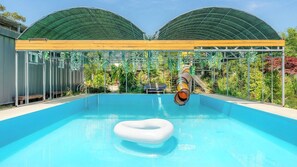 A swimming pool with a slide and a floating ring, surrounded by a covered area with plants. - Gyeongju Yongcheonsu Caravan (Gyeongju)