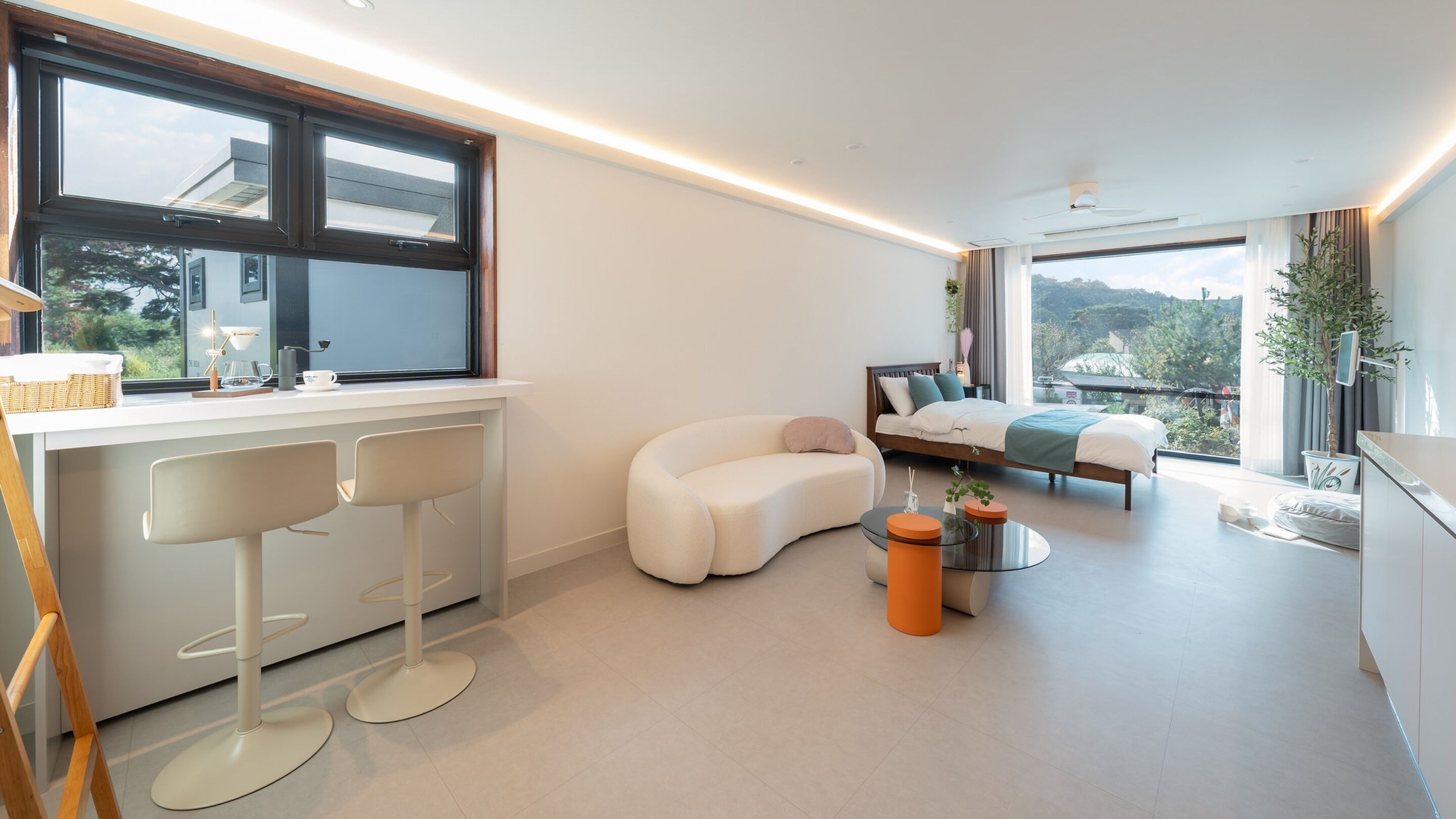A modern bedroom with a large window, a curved sofa, a bed with a view, and a small round table.