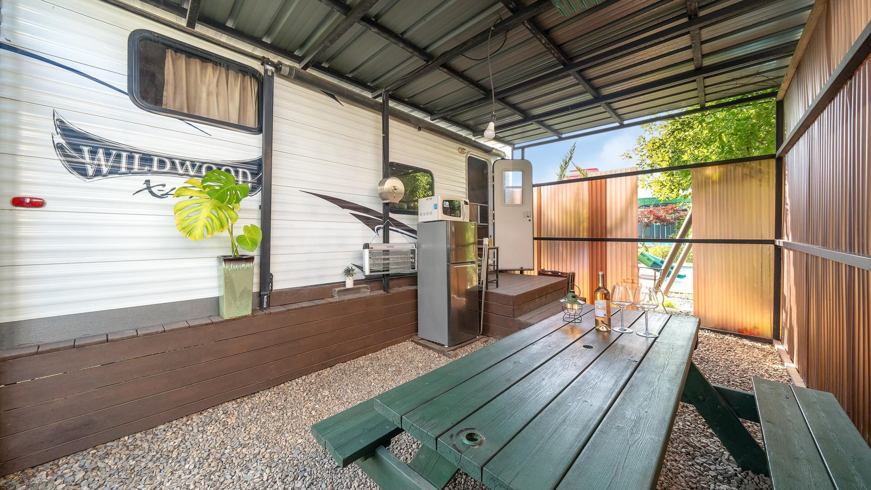 Un espacio exterior cubierto con un banco de madera, un refrigerador y una planta en maceta.
