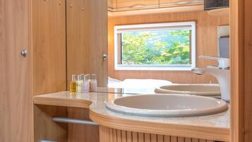 Un baño con tocador de madera, un lavabo y una ventana con vistas a la vegetación.