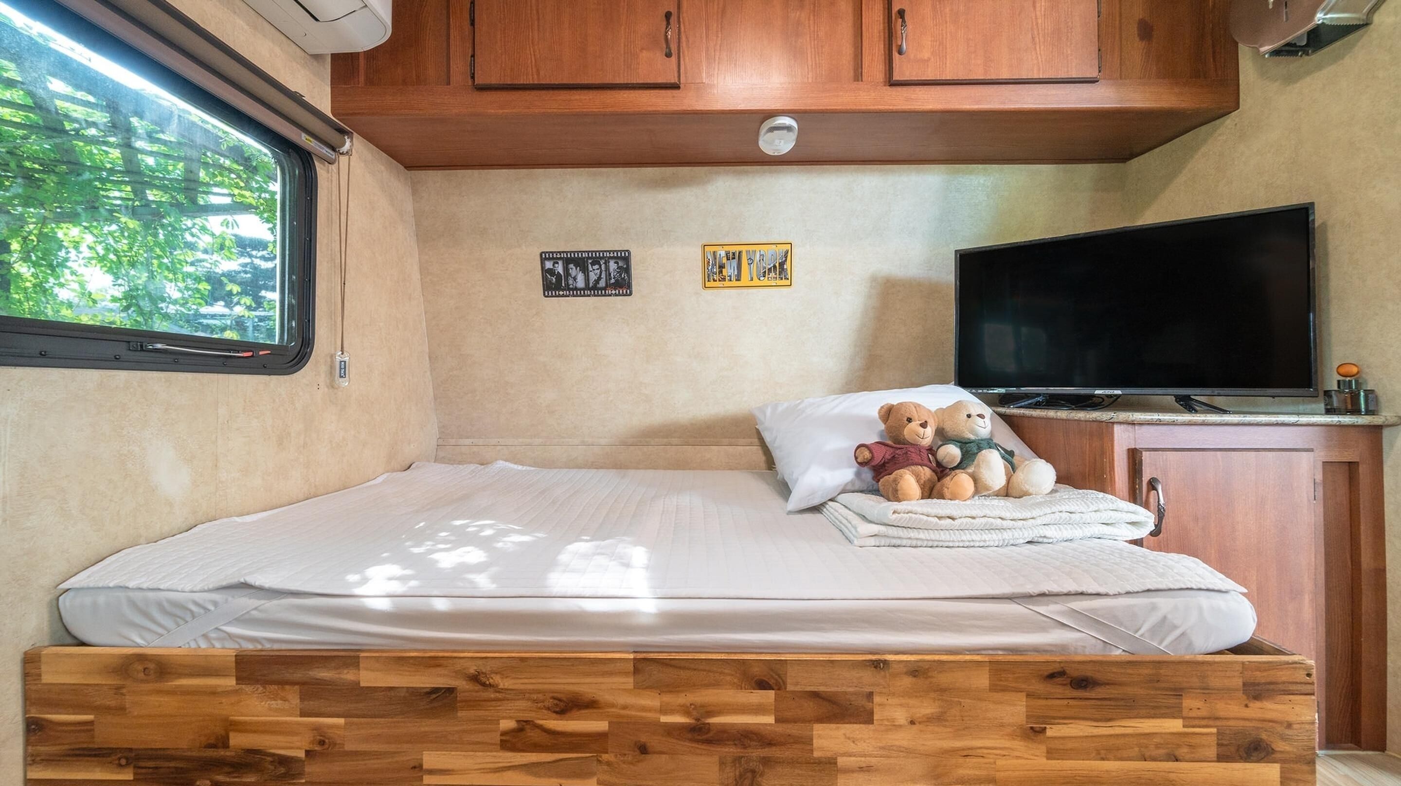 A compact bedroom with a wooden bed frame, a television, and two framed pictures on the wall.