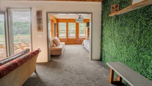 Una habitación acogedora con techo de madera, pared verde, sofá, banco y vistas a una terraza de madera y espacio exterior.