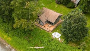 Una casa con un amplio porche, rodeada de árboles frondosos y una masa de agua.