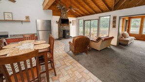 Amplia sala de estar con chimenea de piedra, vigas de madera en el techo y grandes ventanas con vistas al exterior.