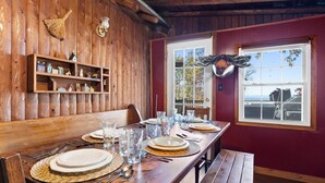 Een houten eettafel gedekt met borden, glazen en bestek, met een houten plank erboven met decoratieve objecten.