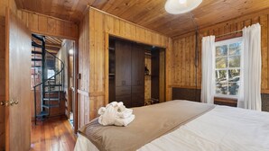Een slaapkamer in een houten hut met een bed, een kledingkast en een spiltrap.