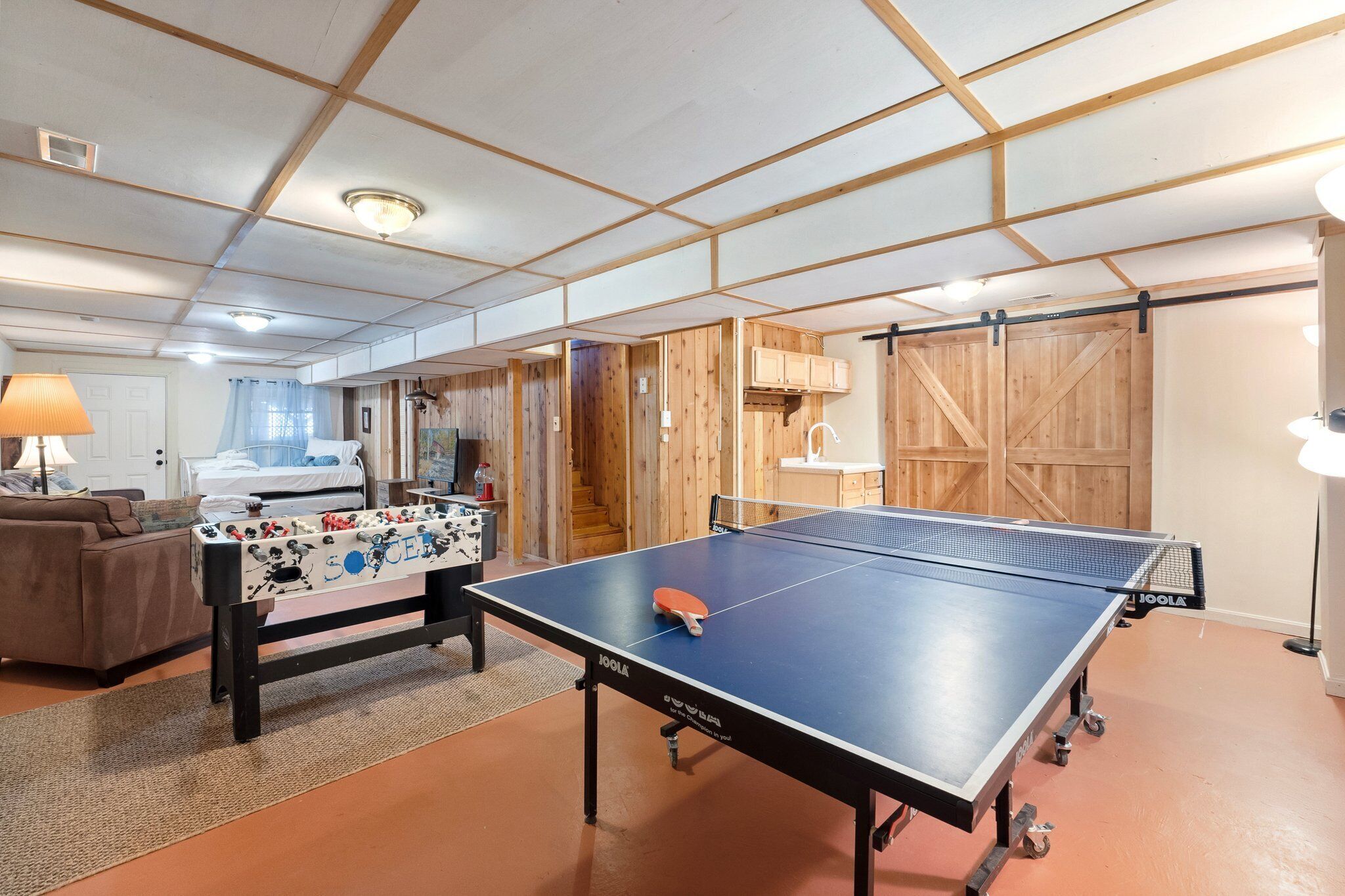 Une pièce avec une table de ping-pong, un baby-foot et un canapé.