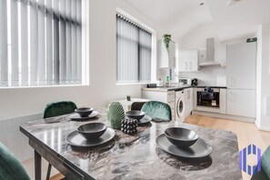 Una cocina moderna con armarios blancos, horno empotrado y comedor con mesa de mármol y cuencos negros.