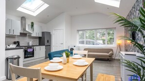 A modern kitchen with skylights, a dining area with a table set for four, and a living area with a sofa and a large window. - Santorini Blues by CEFAS - Free Parking - Bungalow (Greater Manchester)