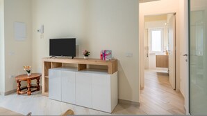 Un salon moderne avec un téléviseur à écran plat posé sur une console en bois, une petite table ronde agrémentée de fleurs et un meuble blanc.