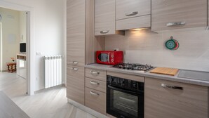 Une cuisine moderne avec des meubles de couleur bois clair, un micro-ondes rouge, une cuisinière à gaz et un four noir.
