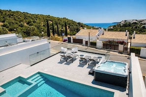 Piscina no terraço com hidromassagem, espreguiçadeiras e vista para o mar.