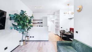 Una cocina moderna con gabinetes blancos, una zona de comedor con un sofá verde y una planta grande en maceta.