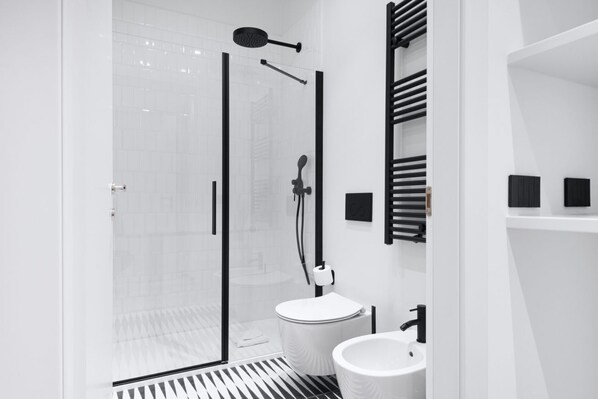 Un baño moderno con ducha envuelta en vidrio, un lavamanos blanco y un toallero negro.