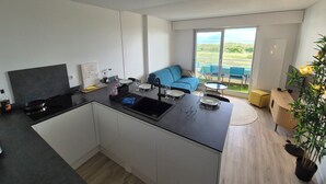 Een moderne keuken met een centraal eiland, een zithoek met een blauwe bank en een balkon met uitzicht op het landschap.