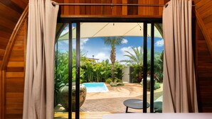 Quarto com vista para uma piscina e plantas tropicais.