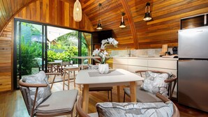 Cozinha moderna com paredes de madeira, área de jantar com mobiliário de vime e uma janela ampla com vista para o verde.