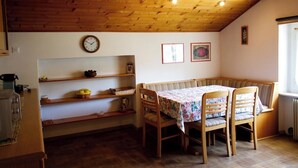Ein gemütliches Zimmer mit Holzboden, einem Esstisch mit Blumenmuster, Holzstühlen, einer Bank und Regalen mit verschiedenen Gegenständen.