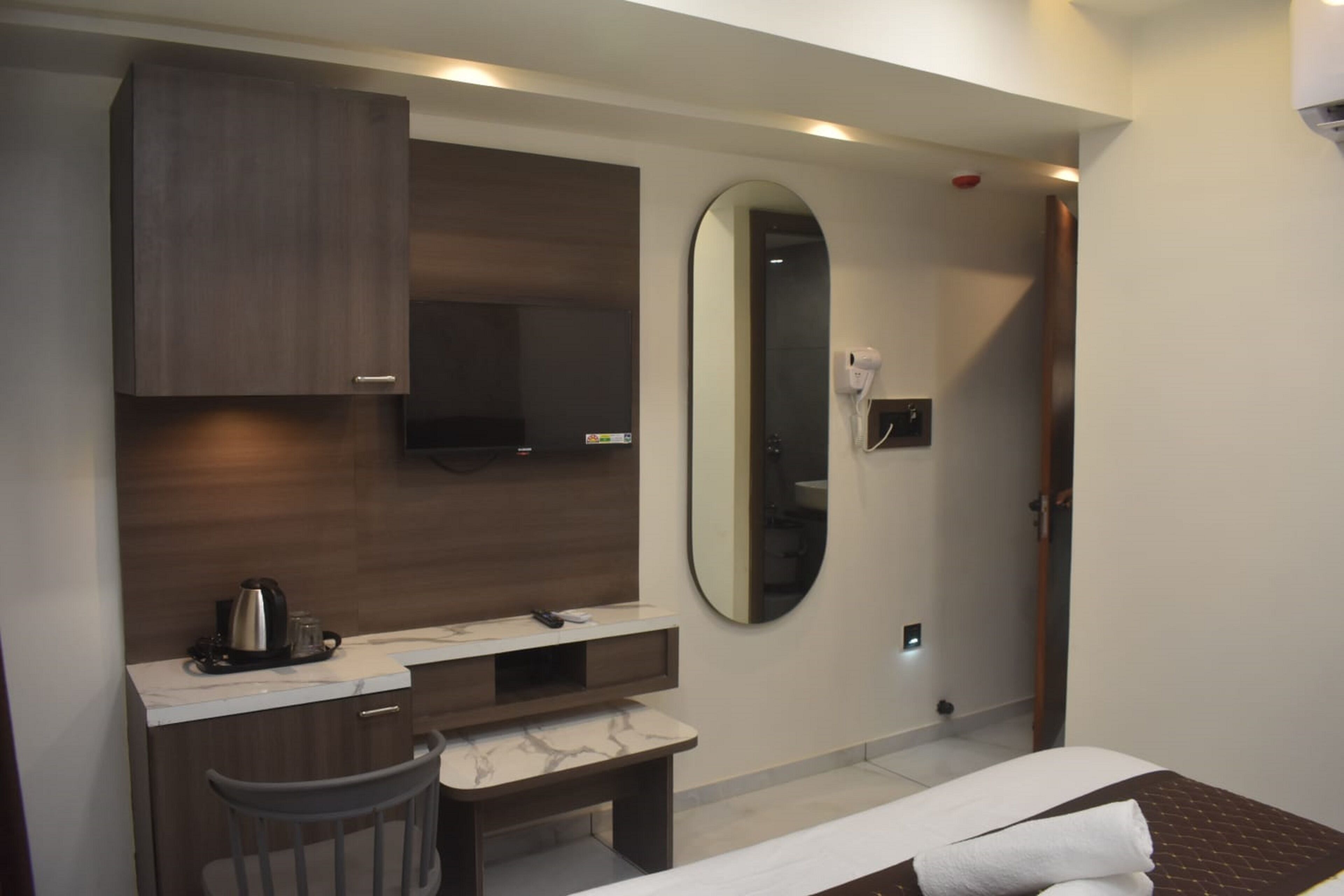 A modern hotel room with a bed, a desk, a chair, a mirror, and a coffee maker.