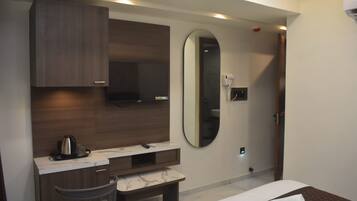 A modern hotel room with a bed, a desk, a chair, a mirror, and a coffee maker.