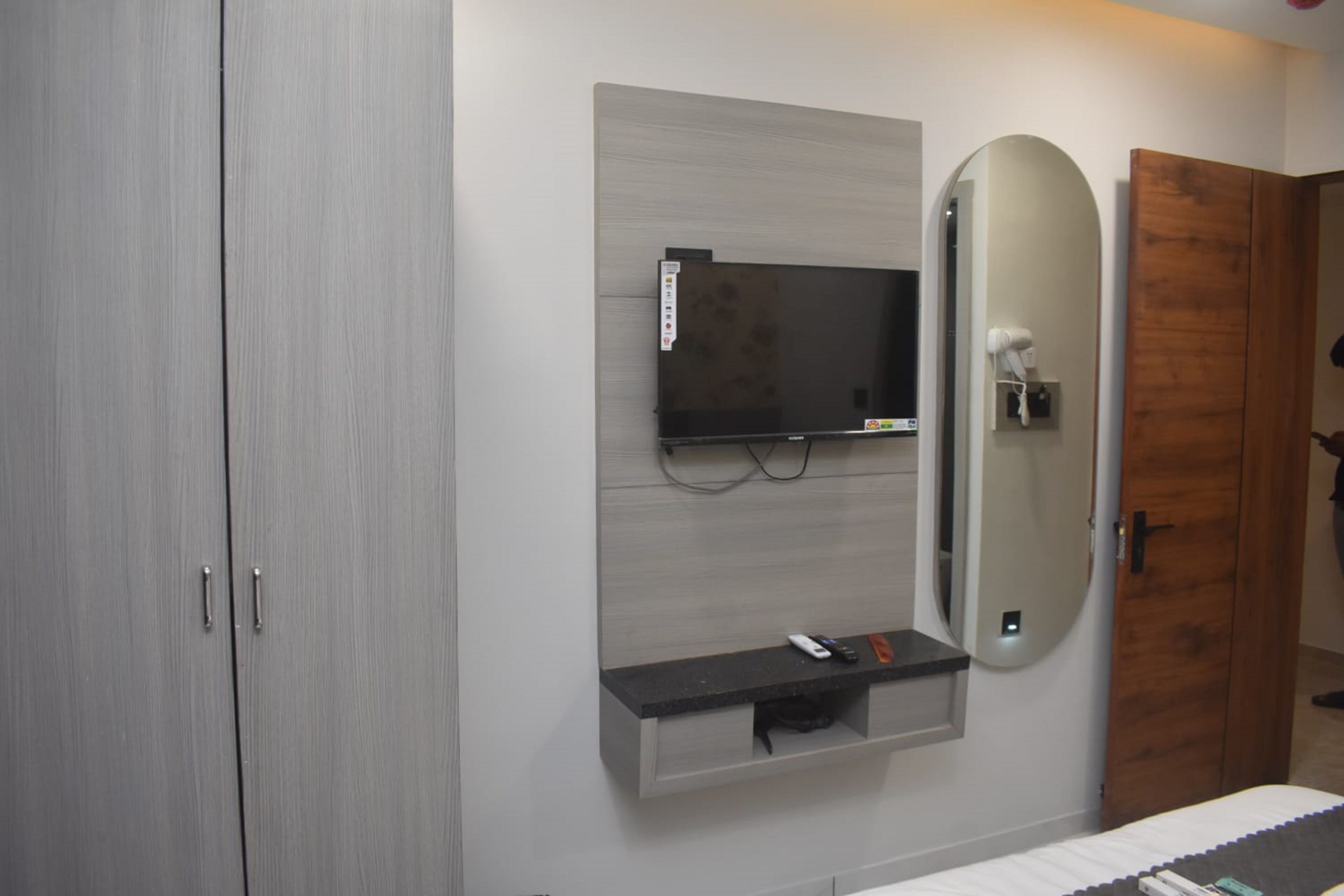 Un baño moderno con un armario gris, televisor montado, tocador con espejo y un perchero para toallas.