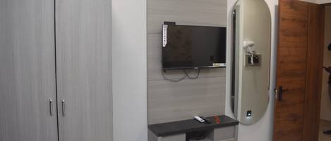 Un baño moderno con un armario gris, televisor montado, tocador con espejo y un perchero para toallas.