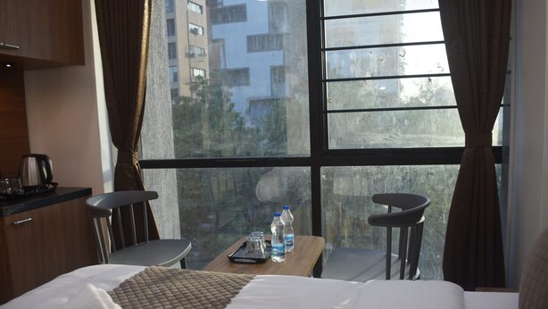 Quarto de hotel com uma cama, uma mesa com garrafas de água, um aparelho de café e duas cadeiras.