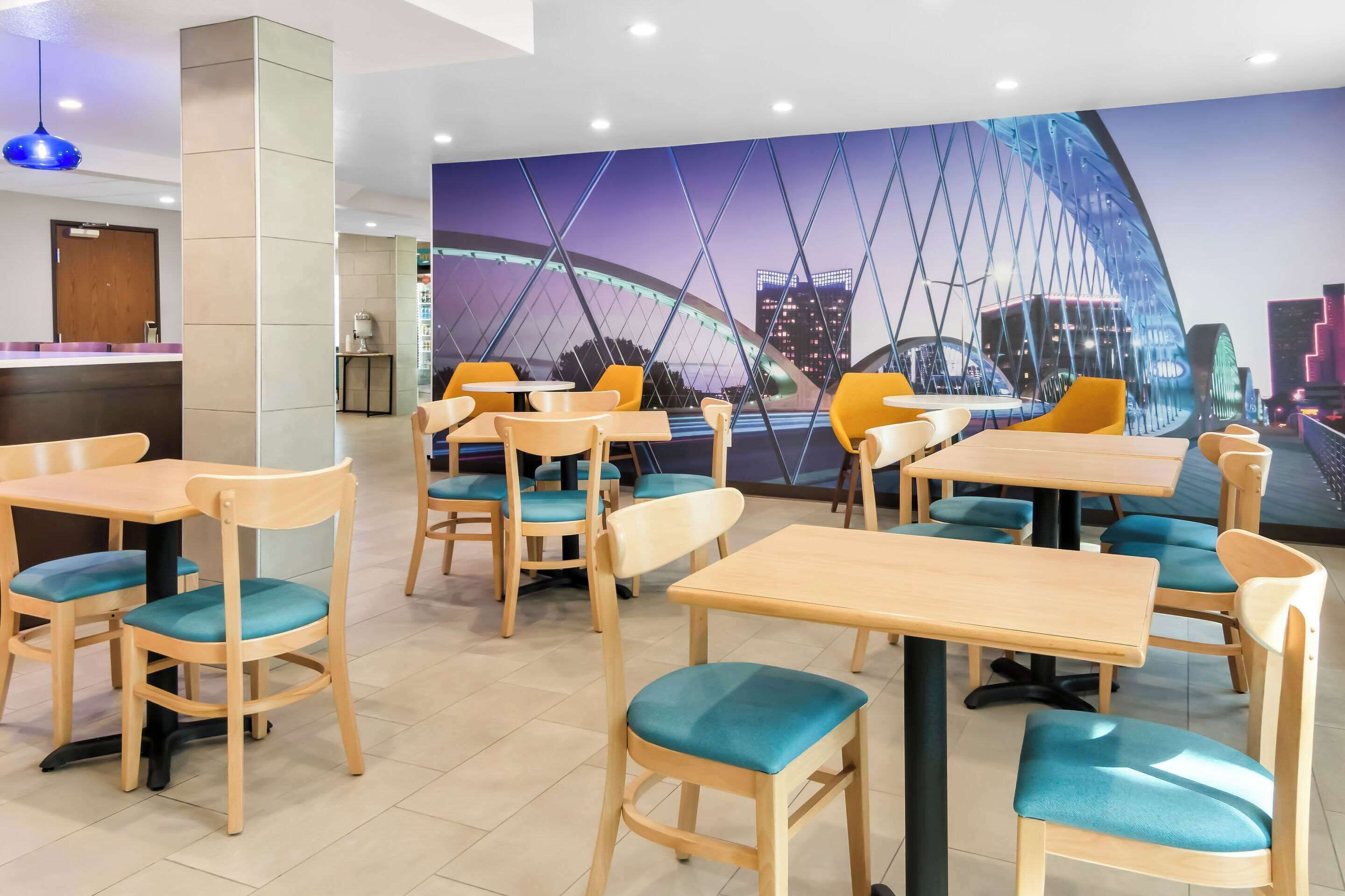 Ein Restaurant mit Holztischen und -stühlen, einem Wandgemälde einer Brücke und Blick auf die Stadt.