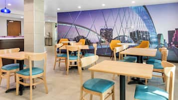 Un ristorante con tavoli e sedie in legno, un murale raffigurante un ponte e vista sulla città.
