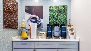 A kitchen counter with coffee and water dispensers, a coffee machine, and a coffee cup. - Clarion Pointe Fort Worth East - Arlington (Fort Worth)