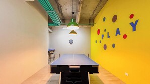 Une table de ping-pong dans une pièce avec un mur jaune et un jeu de fléchettes.