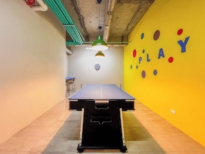 Uma mesa de ping pong em um quarto com parede amarela e um alvo de dardos.