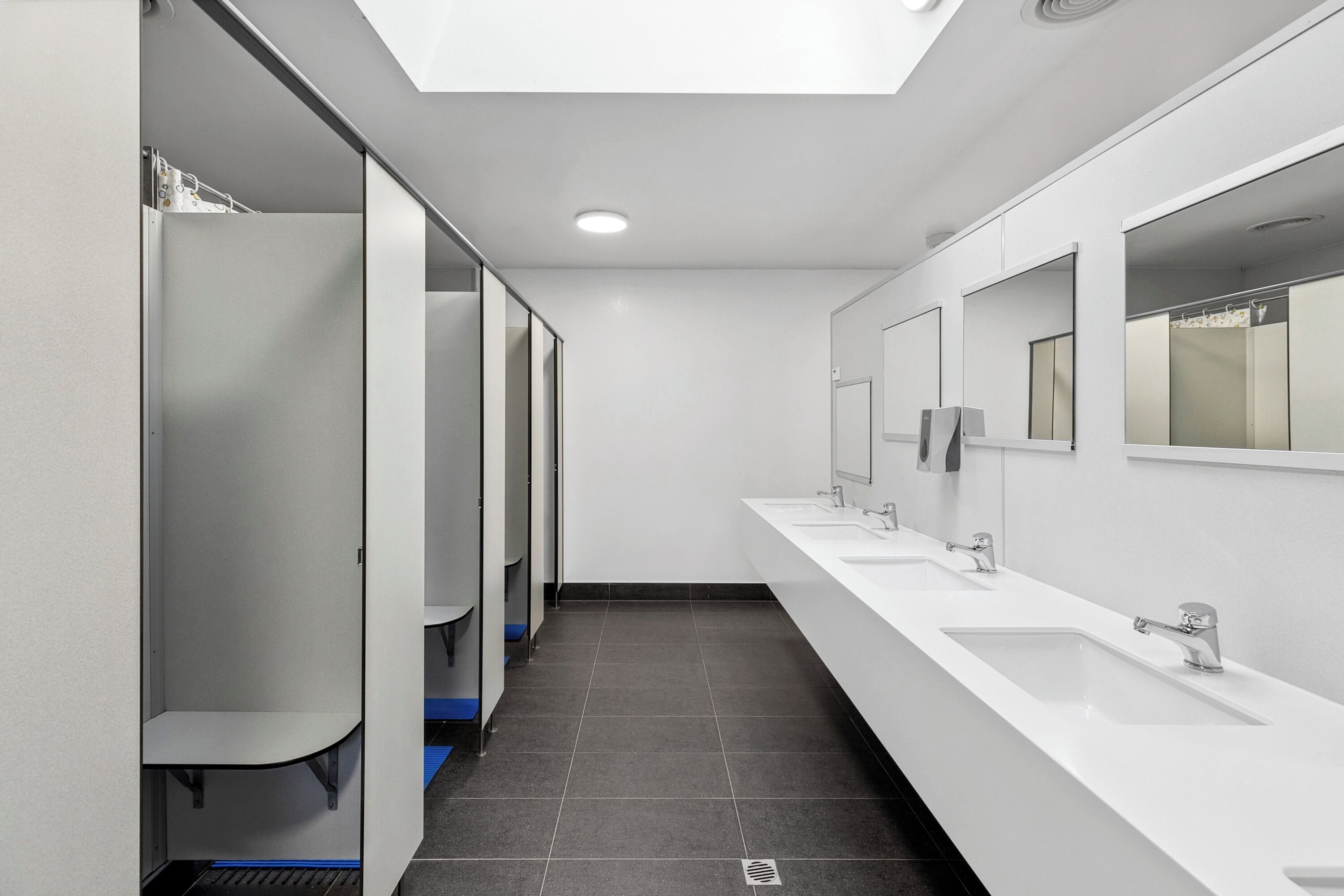 Un baño moderno con varios lavamanos, espejos y cabinas individuales.