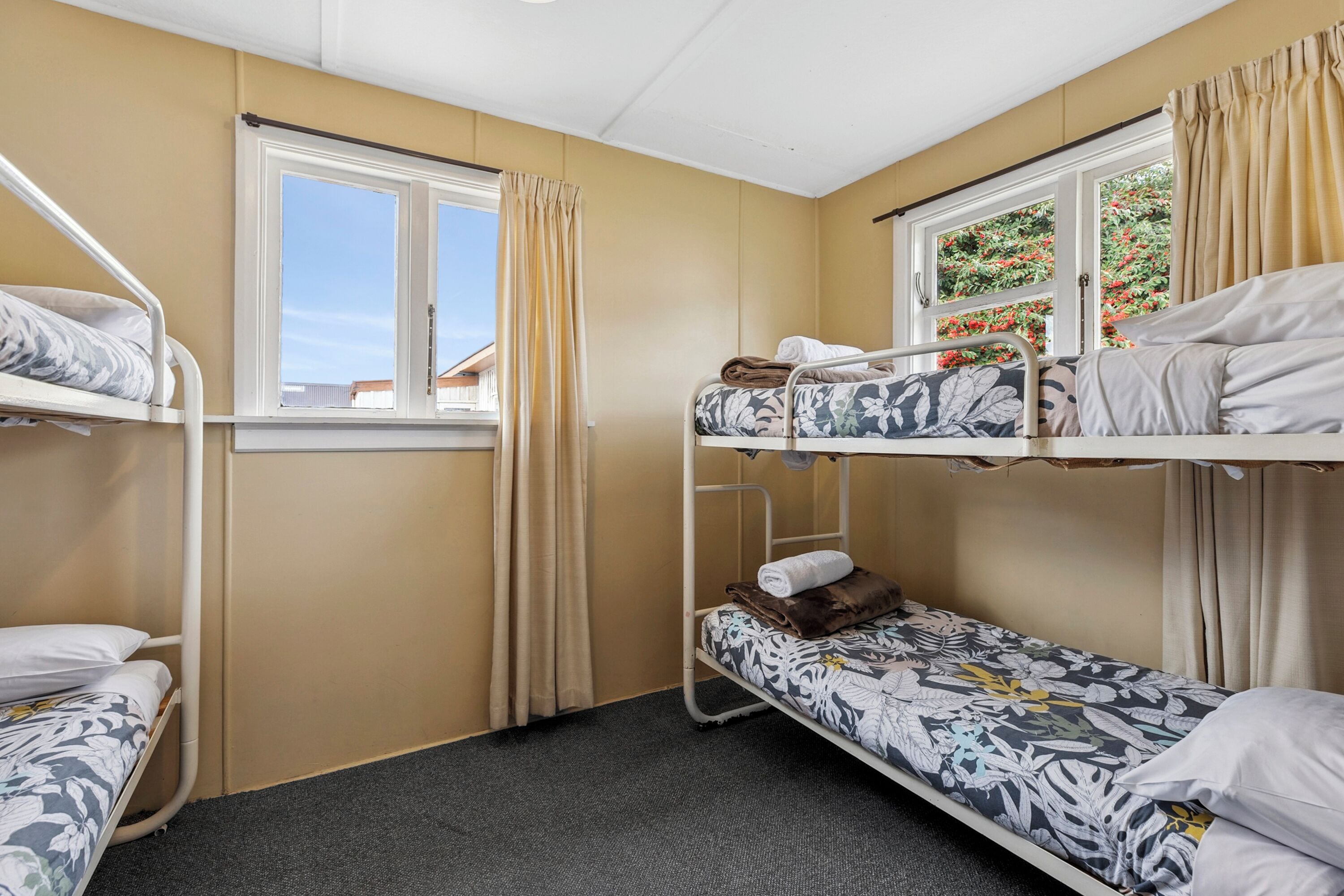 Une chambre de dortoir avec des lits superposés, une fenêtre avec des rideaux et une vue sur la verdure.