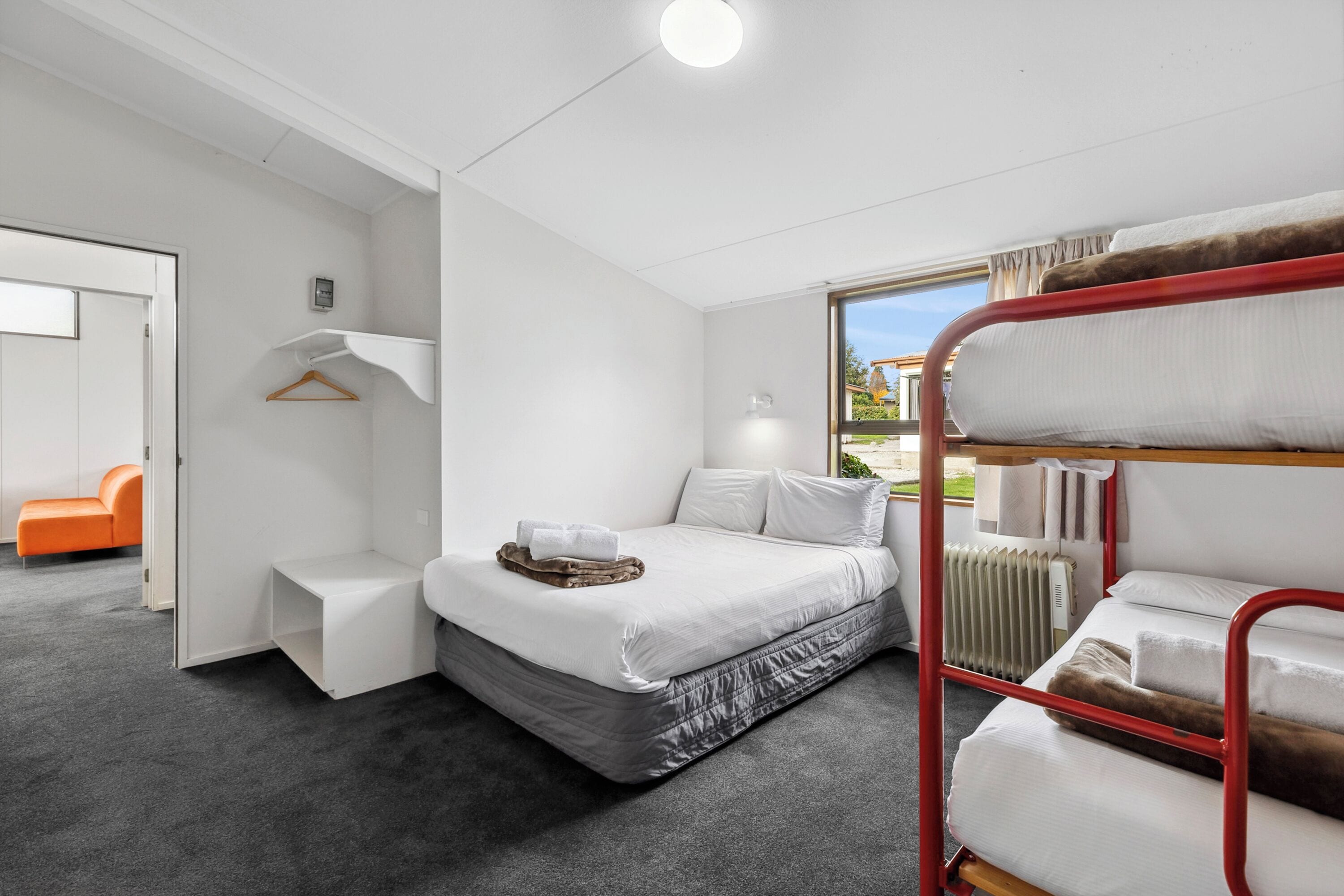 Quarto de hotel compacto com beliche, uma cama individual, um pequeno espaço de estar e vista para o exterior.